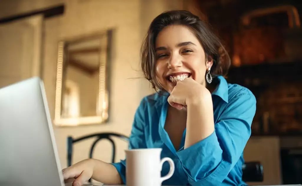donna che sorride in azzurro con tazza caffè davanti al pc
